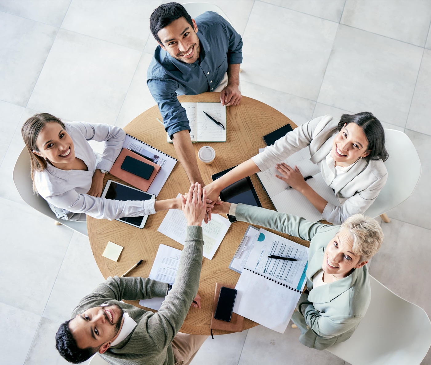 A team's hands stacked over a table of marketing reports — franchisor and franchisee pulling the same direction